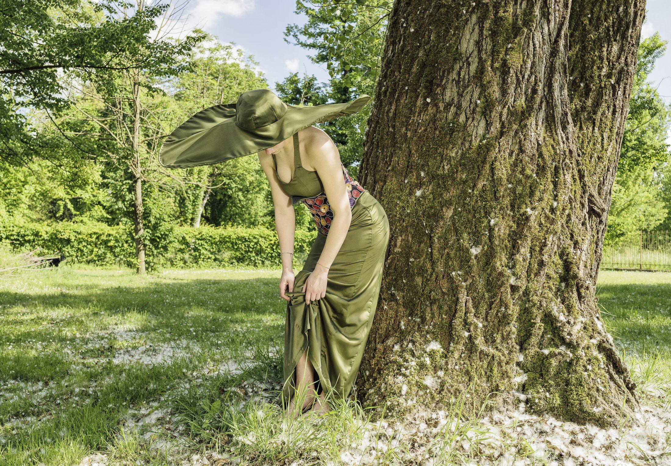 Abito verde oliva, modella chinata sotto un grande albero nel parco